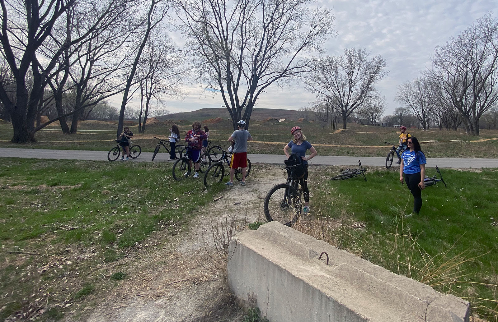 A group of 8 students stand and drink water beside their bicycles as they stop for a break during a site visit to Big Marsh Park