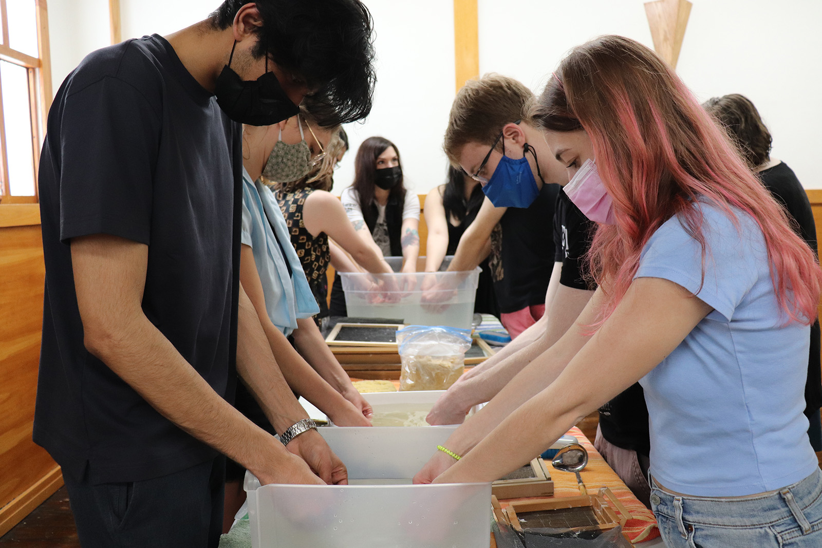 two rows of students wearing face masks face each other and work on a shared tabled space