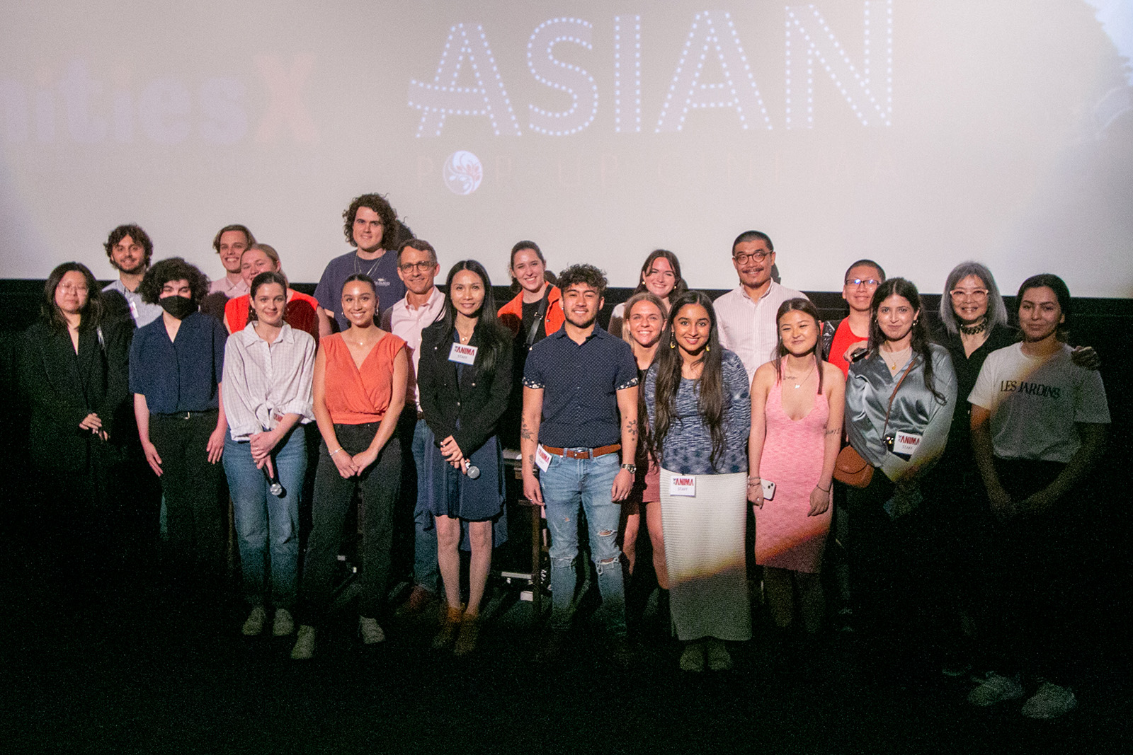 a group of 21 people stand in front of a movie screen that reads "HumanitiesX" and "Asian Pop Up Cinema" 
