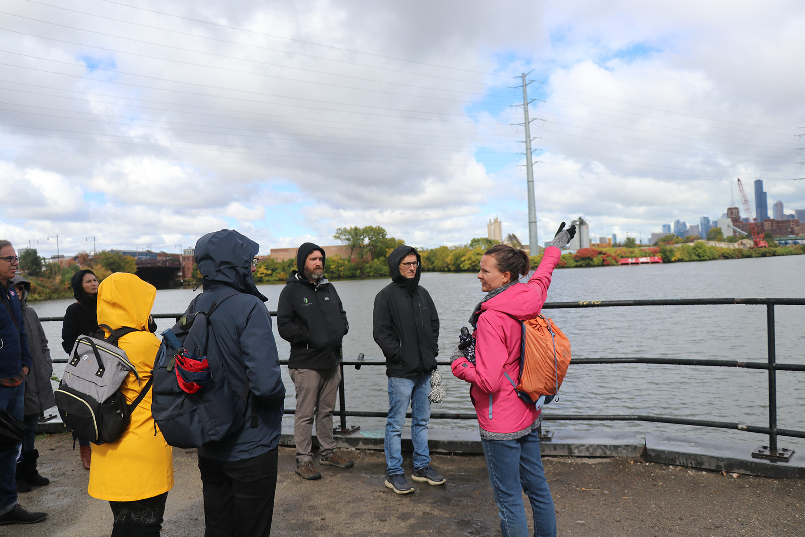 A group of teaching and community fellows stand next to the Calumet River as Beck Lyons gestures toward the water