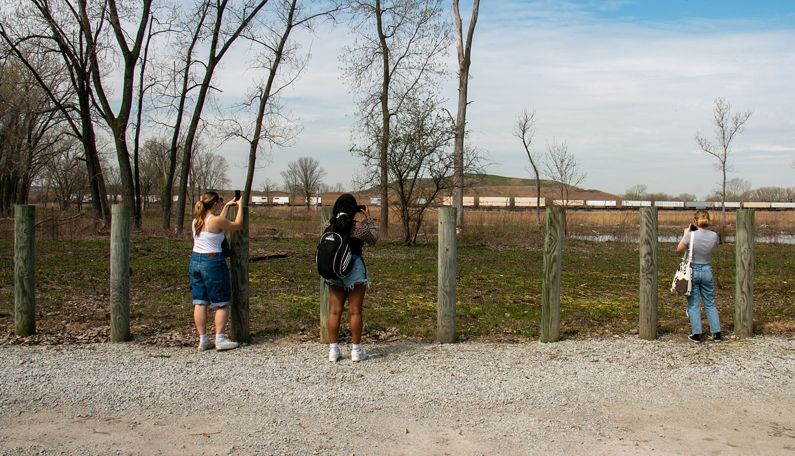 students stand at an old fence in a field taking pictures
