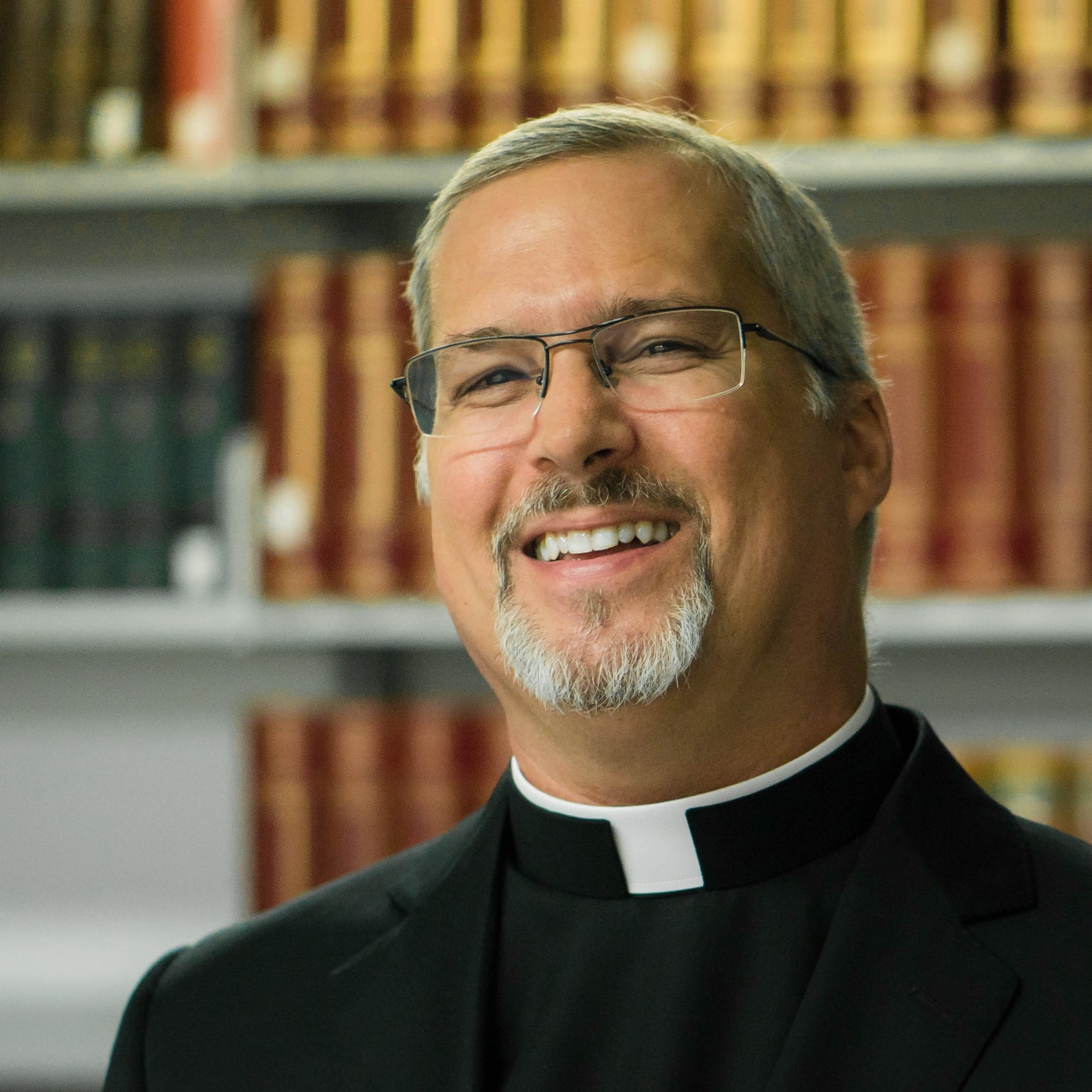Priest in clerical collar in front of bookshelf